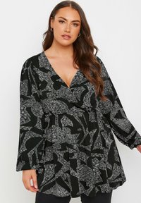 Blouse à motifs noir et blanc avec un décolleté en V, des manches longues et une taille froncée, présentant des formes abstraites et une texture douce.