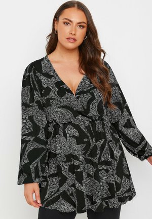 Blusa de patrones en blanco y negro con escote en V, mangas largas y cintura fruncida, que presenta formas abstractas y una textura suave.