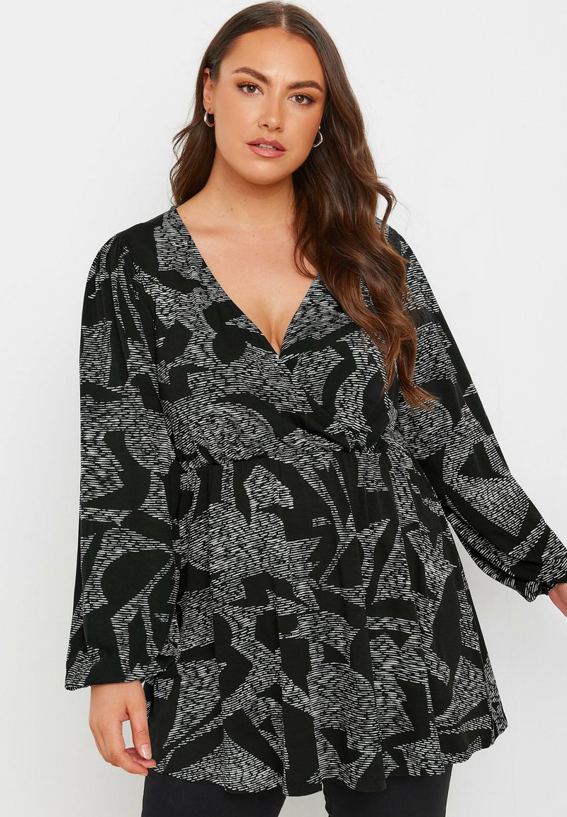 Blouse à motifs noir et blanc avec un décolleté en V, des manches longues et une taille froncée, présentant des formes abstraites et une texture douce.