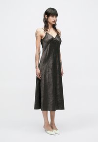 Tumša, kroplēta satīna kleita ar V-veida izgriezumu, plānām lencītēm un plūstošu vidēja garuma dizainu. Valkāta kopā ar baltām smailām kurpēm.