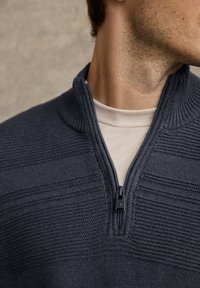 Tmavě šedý pletený svetr s límcem na půl zipu, zdobený strukturovanými proužkovanými vzory a kontrastní světle zbarvenou vnitřní vrstvou.