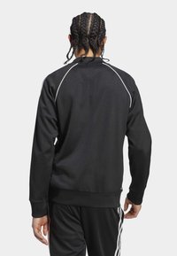 Black athletic sweatshirt with white piping along shoulders, long sleeves, ribbed hem, and smooth texture, paired with matching pants.