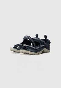 Marina blå sandaler med en texturerad ovandel, dubbla remmar och dragflik. Utrustad med en kraftig grå sula med ett mönster för grepp.