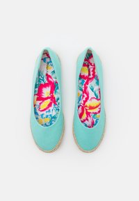 Ballerines en toile bleu clair avec une semelle en espadrille texturée. L'intérieur présente un motif floral coloré avec des accents roses et jaunes.