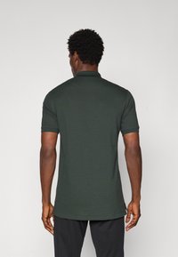 Mørkegrøn polo skjorte med krave, korte ærmer og lige nederste kant. Stoffet ser glat ud med minimale synlige sømme.