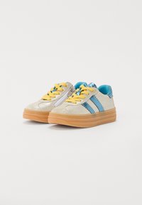 Glittery silver sneakers with blue accents, yellow laces, and a textured gum sole. Features double blue stripes and side zipper.