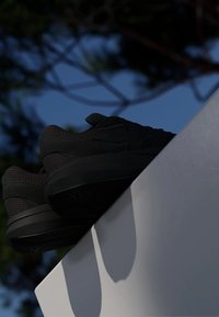 Black sneakers with a textured mesh upper, thick rubber sole, minimalist design, and no visible branding, positioned on a white surface.