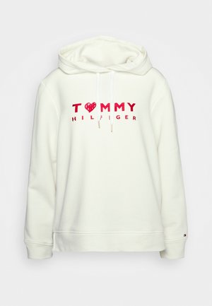 Sudadera blanca con capucha, hecha de una mezcla de algodón, que presenta un corazón rojo y el logotipo "TOMMY HILFIGER" en letras gruesas en la parte frontal. Puños acanalados.