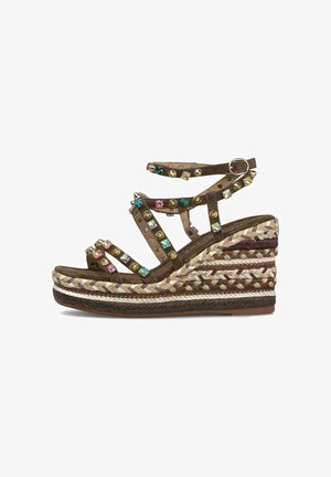 Sandalia de cuña marrón con suela plataforma trenzada, correa con hebilla en el tobillo y adornos de gemas y tachuelas coloridas en varias correas.