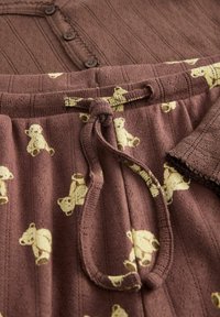 Top in tessuto a coste marrone con bottoni, abbinato a pantaloni marroni con motivo di orsetti gialli e vita con coulisse.