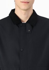Black jacket featuring a corduroy collar, snap-button closure, and a smooth, textured fabric. Design emphasizes simplicity and versatility.