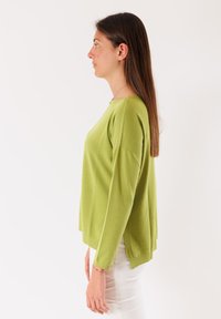 Maglione a maniche lunghe di maglia verde chiaro con colletto tondo, spacchi laterali e polsini a costine; abbinato a pantaloni bianchi.