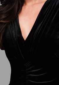 Robe en velours noir avec un décolleté en V profond, une texture douce et des détails froncés à la taille, créant une silhouette ajustée.