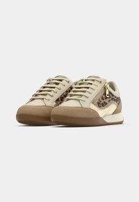 Beige athletic shoes with lace-up design, leopard print accents, metallic details, and a rubber sole. Features a side zipper for easy access.