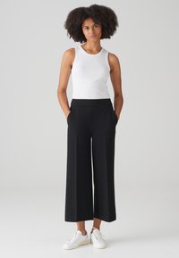 White ribbed tank top paired with high-waisted black wide-leg trousers. Sneakers are white with minimal accents, showcasing a casual look.