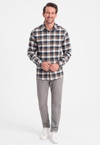 Chemise à carreaux boutonnée avec des couleurs bleu, marron et blanc, à manches longues et ourlet arrondi, assortie à un pantalon gris clair et des baskets blanches.