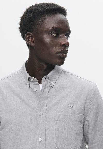Chemise grise à boutons avec un tissu texturé, une poche poitrine et un petit logo brodé. Elle présente un col classique et des poignets à boutons.