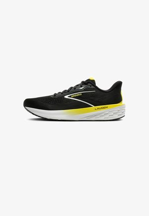 Zapatilla de correr negra con cordones grises y suela blanca. Presenta detalles en amarillo y una parte superior transpirable y texturizada con un logo en el lateral.