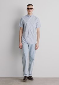 Lichtblauwe kortemouwen overhemd met knopen, gecombineerd met lichtblauwe jeans en donkere zonnebril, met een casual pasvorm en een gladde stoftextuur.