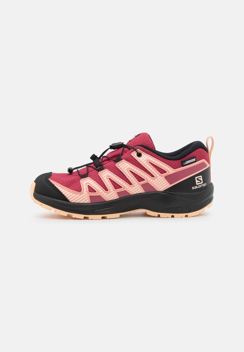 Zapato de trail de malla roja y rosa con acentos negros, superficie texturizada y suela flexible. Cuenta con un sistema de cordones integrado y un tirador en el talón.
