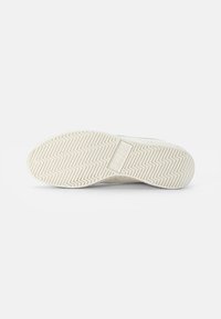 Semelle de sneaker blanche avec une surface en caoutchouc texturé, présentant un motif en zigzag et un logo embossé sur le côté. Bords lisses, design minimal.
