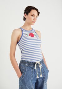 Modra in bela črtasta majica s tankimi naramnicami z grafiko rdeče jabolke, ki ima prilegajoč kroj, v kombinaciji z ohlapnimi denim hlačami.
