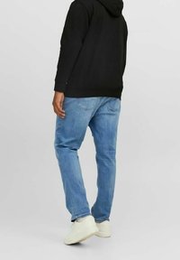 Jeans in denim azzurro, a taglio dritto, con un lavaggio sbiadito e tasche posteriori. Abbinati a una felpa con cappuccio nera e sneakers bianche.