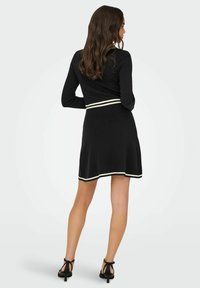 Crna haljina s dugim rukavima, uskim tijelom i raširenim suknjom. Ima bijele horizontalne pruge na struku i rubu. Glatka, meka tekstura.