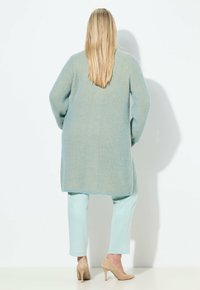 Hellblaue Strickjacke mit langen Ärmeln und lockerem Schnitt, kombiniert mit hellmintgrünen Hosen und beigen High Heels.