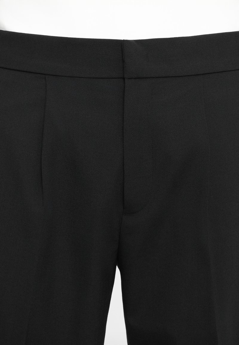 Black trousers with a smooth fabric texture, featuring front pleats, a flat waistband, and no visible hardware or pockets.