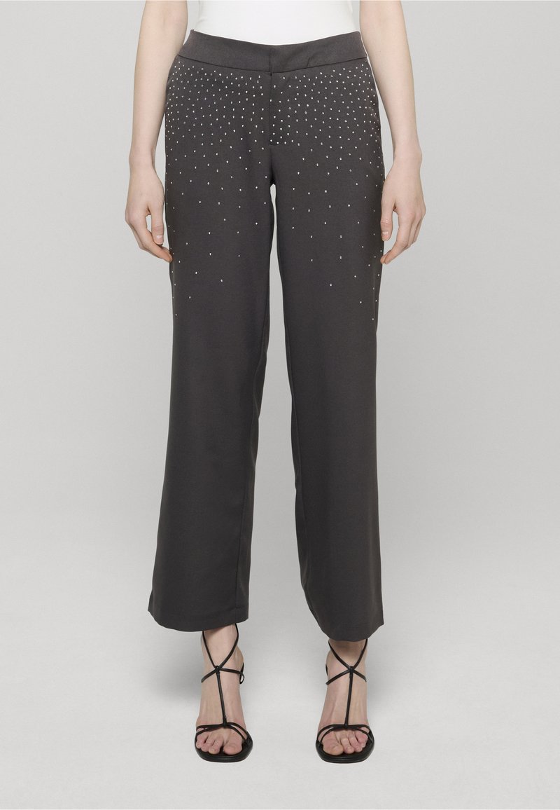 Szare spodnie o szerokich nogawkach z ozdobami złożonymi ze srebrnych ćwieków ułożonych w gradientowy wzór, z płaskim pasem i gładką teksturą materiału.