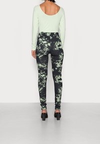 Ljus mintgrön långärmad topp med låg rygg, kombinerad med svarta leggings med ett grönt tie-dye mönster och svarta högklackade skor.