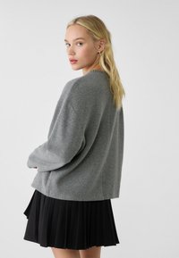 Grauer Oversized-Pullover mit langen Ärmeln, Rundhalsausschnitt und gerippten Kanten, kombiniert mit einem fließenden schwarzen plissierten Rock.