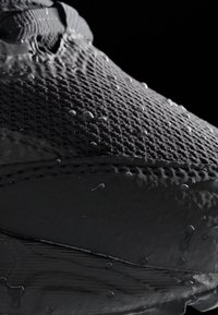 Zwarte sportieve schoen met een gestructureerde mesh bovenkant, voorzien van waterdruppels op het oppervlak. Soepele accenten en gestikt detail zichtbaar.
