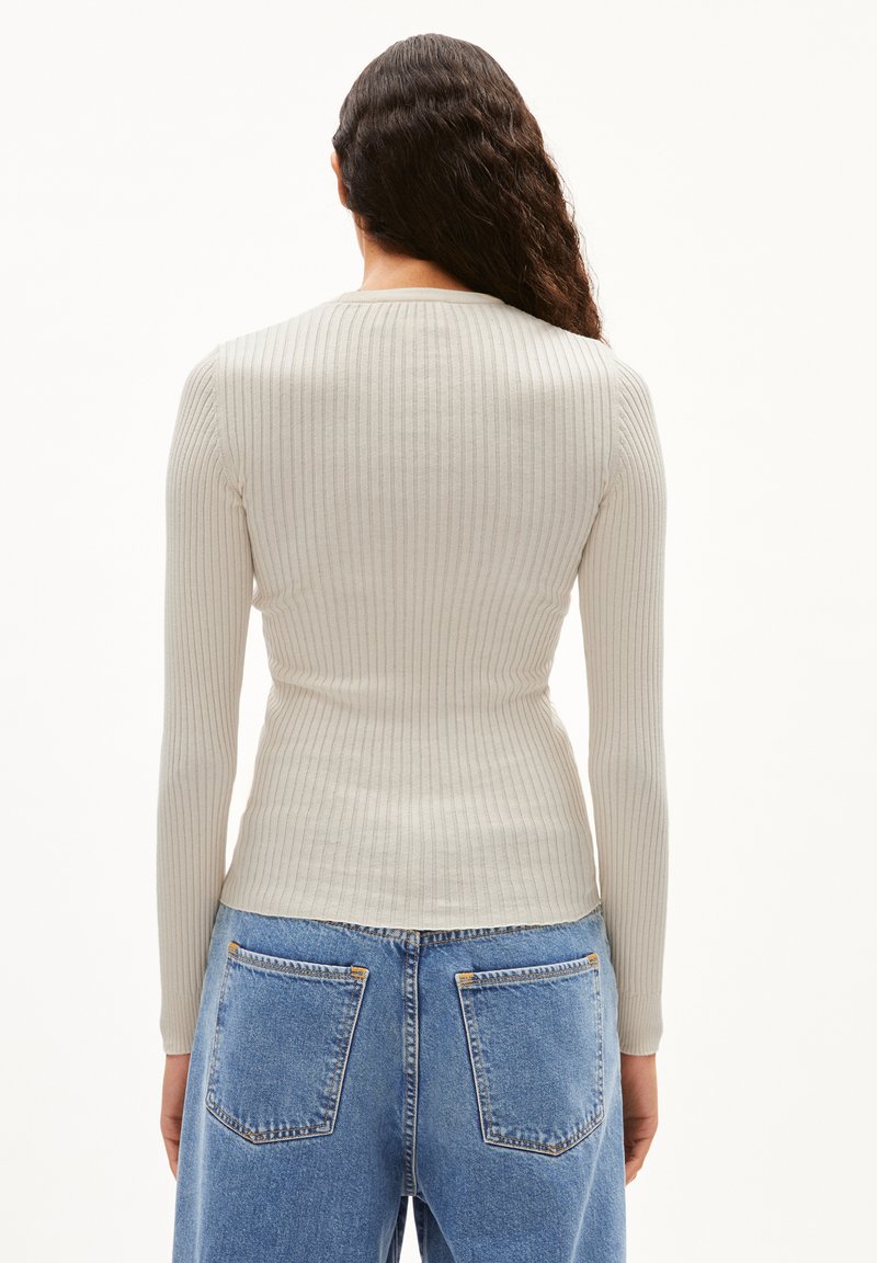 Rippiger, hellbeiger Pullover mit langen Ärmeln und taillierter Passform, kombiniert mit hochgeschnittenen blauen Denim-Jeans mit Gesäßtaschen.