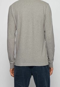 Mörkgrå långärmad t-shirt av mjuk bomullsblandning, med rund hals och enkel textur, kombinerad med mörka kordbyxor.