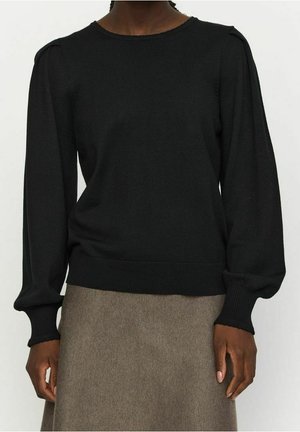 Person wearing a black long-sleeve blouse with puffed sleeves and ribbed cuffs, paired with a brown skirt.