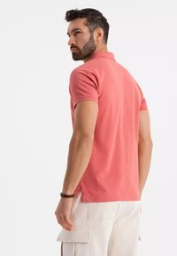 Lyhythihainen polo-paita korallinvärisenä, valmistettu puuvillasta. Ominaisuuksiin kuuluvat klassinen kaulus, sivuventtiilit ja vartalonmyötäinen muotoilu, joka sopii rentoon pukeutumiseen.