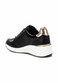Zapatilla negra de cuero sintético perforado, con acentos dorados en el talón y los laterales, y una suela blanca gruesa. Incluye cordones y un cuello acolchado.