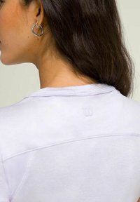 Camiseta blanca con una textura suave, que presenta una costura cosida y un pequeño logo en relieve en la parte posterior, debajo del escote.