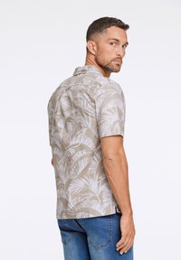Korte mouw shirt van beige stof met grote witte bladvormen. Voorzien van een kraag en een rechte zoom, gecombineerd met blauwe jeans.