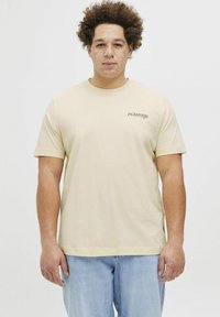 Beige puuvillane t-särk lühikeste varrukatega, ümar kaelus ja väike logo vasakul rinnal. Seljas helesinised teksad.