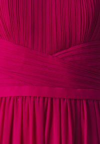 Rochie fuchsia cu pliuri verticale, având o talie lată și un material moale, fluid care se lasă în straturi plisate. 