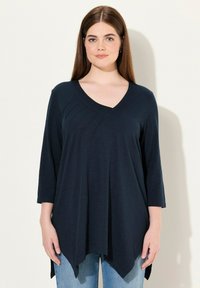 Marinblå V-ringad topp med trekvartslånga ärmar, rundad nederkant och diskreta veck fram. Tillverkad i ett lätt, texturerat tyg.