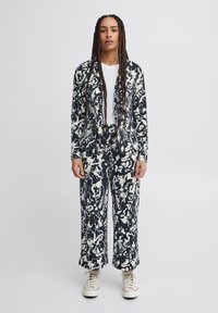 Patterned suit featuring a navy and cream abstract design; made of soft fabric, with a jacket and wide-leg pants. Worn with a white t-shirt.