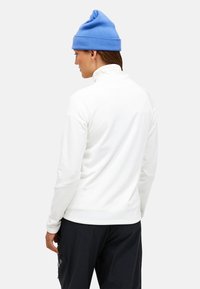 Pullover bianco con colletto alto e maniche lunghe. Berretto di lana blu. Design semplice con texture liscia, senza motivi o accessori visibili.