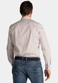 Heren overhemd met lange mouwen in het wit met kleine blauwe en rode bloemenprint. Gecombineerd met donkerblauwe jeans en een zwarte geweven riem.