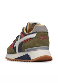 Sneaker verde in suede con accenti blu e rossi, caratterizzato da un logo bianco, suola in gomma e dettagli testurizzati. Tallone imbottito a contrasto.