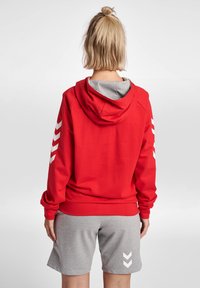 Sweat à capuche rouge avec doublure grise, comportant des motifs en chevron blanc sur les manches. Assorti à un short gris, présentant une coupe décontractée.