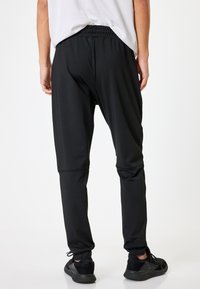 Sorte atletiske track bukser med elastisk talje og snøre. Har tapered ben og blødt, glat stof med en let glans.
